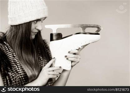 Winter sport activity concept. Girl wearing warm hat and furry waistcoat holding and looking at ice skate, black and white studio shot.. Woman wearing winter hat looking at ice skate