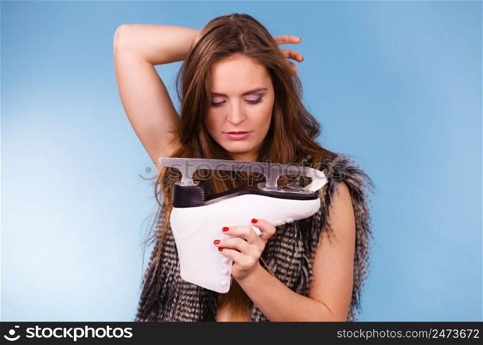 Winter sport activity concept. Woman holding ice skate poiting at blade, blue background studio shot.. Woman holding ice skates, winter sport
