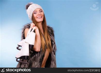 Winter sport activity concept. Woman wearing furry warm hat holding ice skate, blue background studio shot.. Woman holding ice skates, winter sport