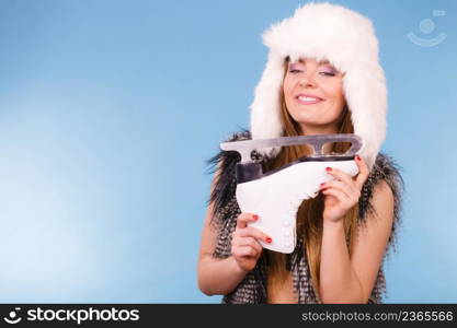 Winter sport activity concept. Woman wearing furry warm hat holding ice skate, blue background studio shot.. Woman holding ice skates, winter sport