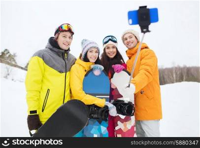 winter sport, leisure, friendship, technology and people concept - happy friends with snowboards and smartphone taking selfie