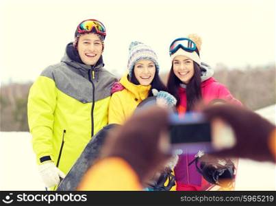 winter sport, leisure, friendship, technology and people concept - happy friends with snowboards and smartphone taking picture