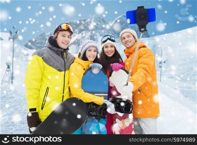winter sport, leisure, friendship, technology and people concept - happy friends with snowboards and smartphone taking selfie over snow and mountain background