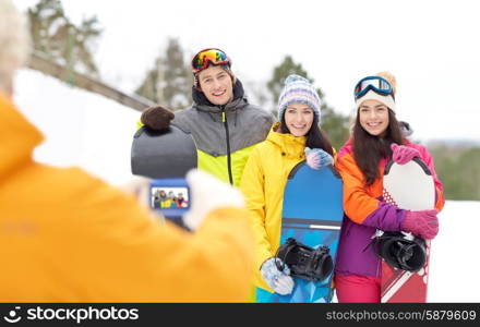 winter sport, technology, leisure, friendship and people concept - happy friends with snowboards and smartphone taking picture outdoors