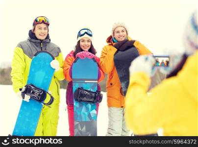 winter sport, technology, leisure, friendship and people concept - happy friends with snowboards and smartphone taking picture outdoors