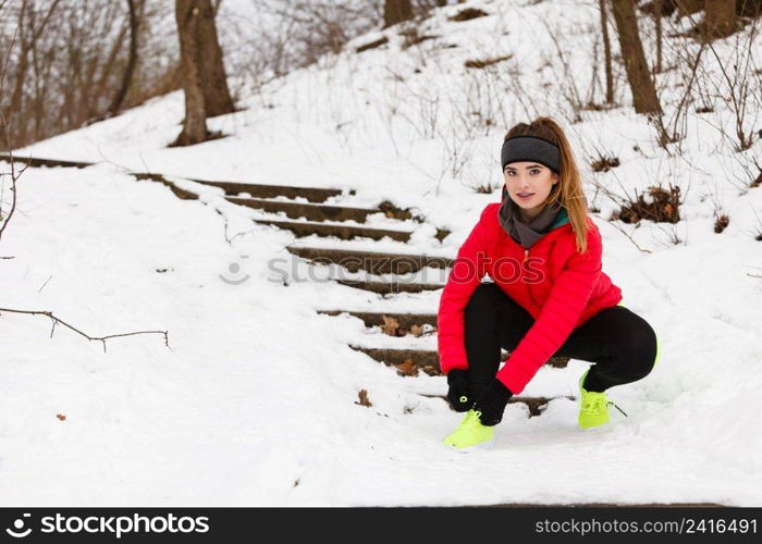 Winter sports fashion concept. Woman tying sport fitness shoes in snow, footwear for workout outside. Woman tying sport shoes during winter