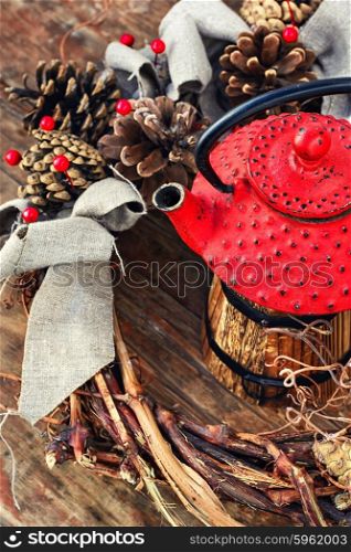 Winter still life with tea. Retro red cast iron kettle and cane wreath with cones