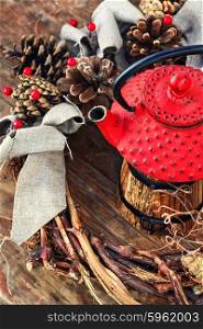 Winter still life with tea. Retro red cast iron kettle and cane wreath with cones