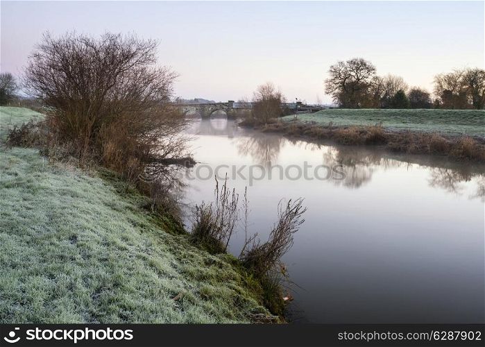 Winter sunrise landscape over river and fields covered in frost