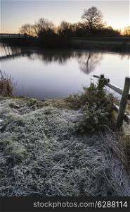 Winter sunrise landscape over river and fields covered in frost