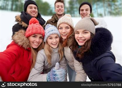 winter, technology, friendship and people concept - group of smiling men and women taking selfie and showing thumbs up outdoors