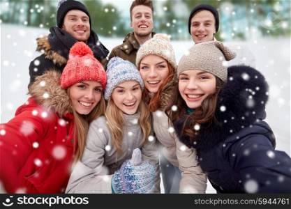 winter, technology, friendship and people concept - group of smiling men and women taking selfie and showing thumbs up outdoors