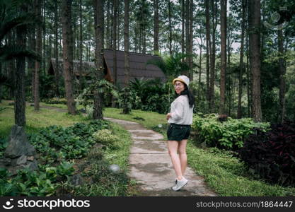 Winter travel relax vacation,Portrait Asian female tourist in white dress with hat stands in pinewood cabin in pine forest green on nature trail at Doi Bo Luang Forest Park,Chiang Mai, Thailand