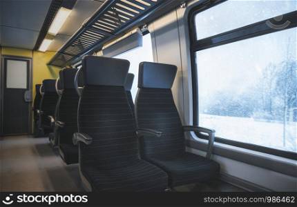 Winter traveling concept with a german train interior with black seats, in a row, and a window view with a snowy nature landscape, on a snowstorm.