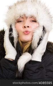 Winter vacation. Cheerful positive girl in warm clothes. Happy young woman in fur hat blowing a kiss isolated on white.