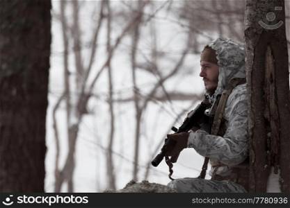 Winter war in the Arctic mountains. Operation in cold conditions. Soldier in winter camouflaged uniform in Modern warfare army on a snow day on forest battlefield with a rifle. Selective focus. High-quality photo. Winter war in the Arctic mountains. Operation in cold conditions.Soldier in winter camouflaged uniform in Modern warfare army on a snow day on forest battlefield with a rifle. Selective focus