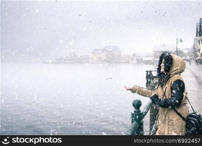 Winter weather theme image with a young woman smiling and holding hand to catch snowflakes, by the Hallstatter lakeshore, in Hallstatt village, Austria.