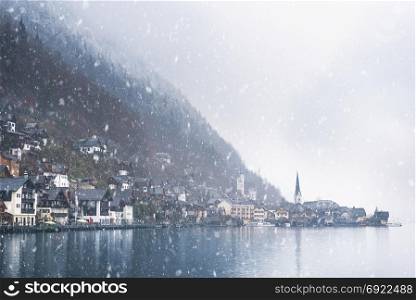 Winter weather theme image with the famous Hallstatt market town, surrounded by the Alps mountains and the Hallstatter lake, on a snowy day of November.