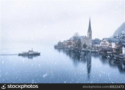 Winter weather theme image with the famous touristic town, the Hallstatt, located on the Hallstatter lakeshore, in Austria, on a snowy day of November.