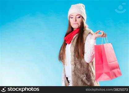 Winter woman in warm clothes with red paper shopping bag on blue. Funny girl buying. Sale and retail.