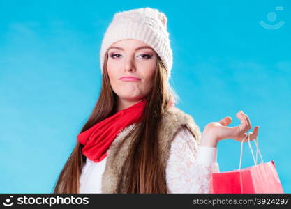 Winter woman in warm clothes with red paper shopping bag on blue. Funny girl buying. Sale and retail.