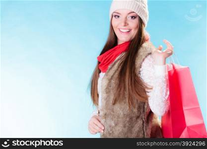 Winter woman in warm clothes with red paper shopping bag on blue. Girl buying. Sale and retail.