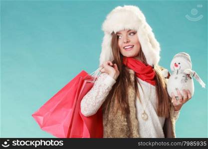 Winter woman with little snowman and bags shopping. Woman with little snowman and bags shopping. Young girl in fur hat in studio blue. Winter fashion clothes sale.