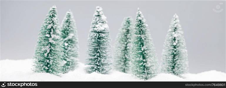 Winter wonderland with small decorative fir trees at snowfall, winter holidays concept. Christmas fir trees at snowfall