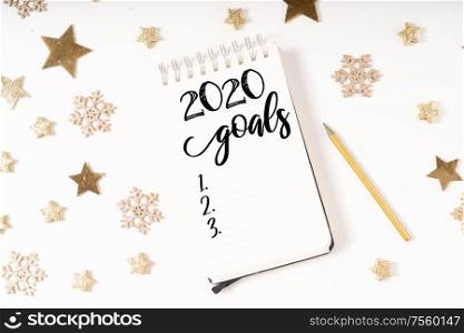 Wish list for Cristmas and 2020 New Year. Holiday decorations and ruled notebook with wish list on white desk, flat lay. Christmas flat lay scene with golden decorations