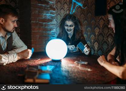 Witch reads a magic spell over a crystal ball, young couple on spiritual seance. Female foreteller calls the spirits. Witch reads a magic spell over a crystal ball