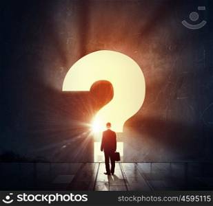 With doubts about future. Back view of businessman standing in light of big question mark