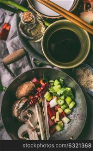 Wok with chopped vegetables and spices on kitchen table background with chopsticks, soy sauce and sesame oil. Asian food , Chinese or Thai cuisine concept