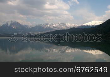 Wolken im Zeitraffer nber einem Gebirgssee. Im Hintergrund die schneebedekten Berge.