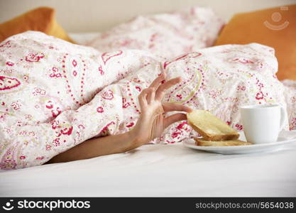 Woman&#39;s Hand Reaching From Under Duvet For Breakfast