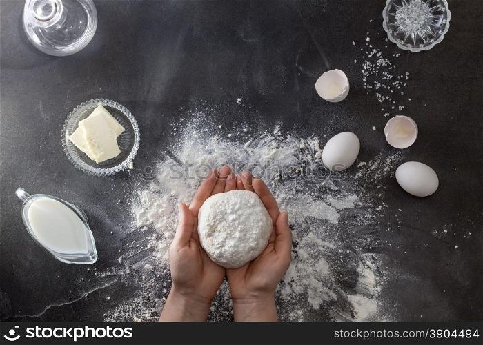 Woman&#39;s hands knead dough on table with flour and ingridients. Top view.