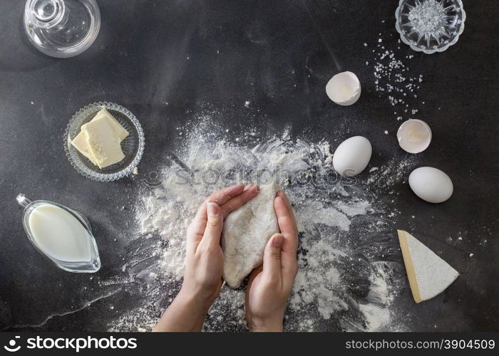 Woman&#39;s hands knead dough on table with flour and ingridients. Top view.