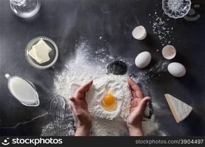 Woman&#39;s hands knead dough on table with flour, eggs and ingridients. Top view.