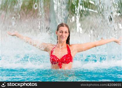 woman a public swimming pool standing under a water gadget