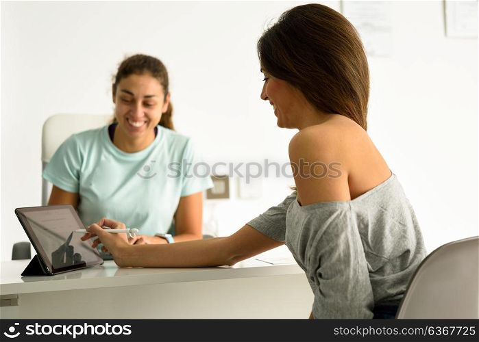 Woman accepting and signing her diagnosis with female physiotherapist. Brunette patient having consultation in physiotherapy center.