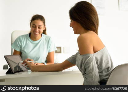 Woman accepting and signing her diagnosis with female physiotherapist. Brunette patient having consultation in physiotherapy center.