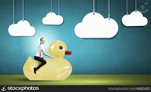 Woman acting like child. Young happy businesswoman riding yellow rubber duck