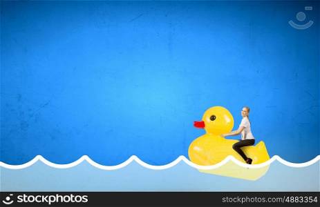 Woman acting like child. Young happy businesswoman riding yellow rubber duck