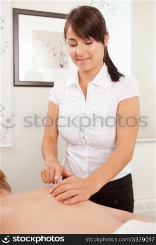 Woman acupuncturist using an insertion tube to place a needle in a female patient.