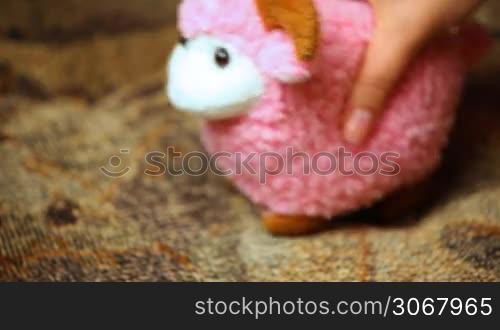 woman&acute;s hand playing toy pink sheep on couch closeup