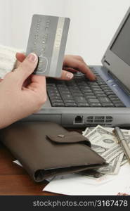 Woman&acute;s hand with credit card at laptop. Bills, money, checks on table beside her. Shot in studio.