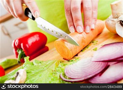 Woman&acute;s hands cutting carrot, behind fresh vegetables.
