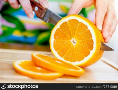 Woman&acute;s hands cutting fresh orange on kitchen