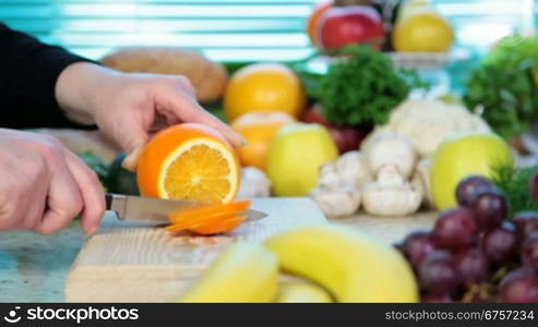 Woman&acute;s hands cutting fresh orange on kitchen