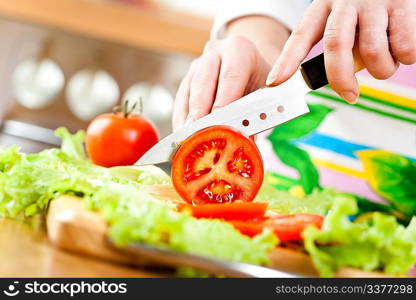 Woman&acute;s hands cutting tomato, behind fresh vegetables.