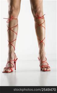 Woman&acute;s legs and feet wearing sexy red high heel shoes that lace up to her knees.